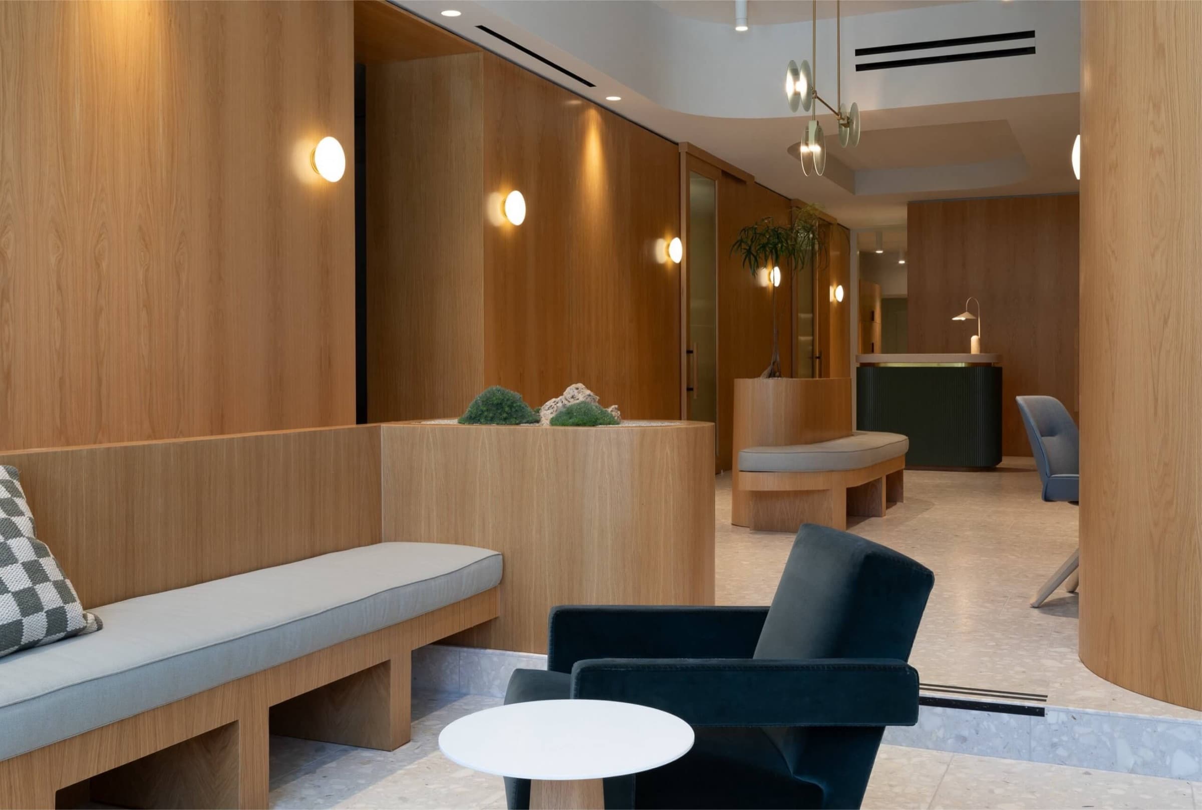 Clover interior — a white-oak reception lounge with a built-in bench, terrazzo floor, and a moss-and-stone planter