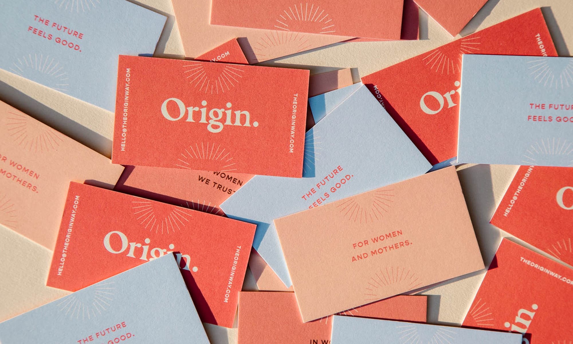 A scattered pile of Origin business cards in coral, ember, powder blue, and cream